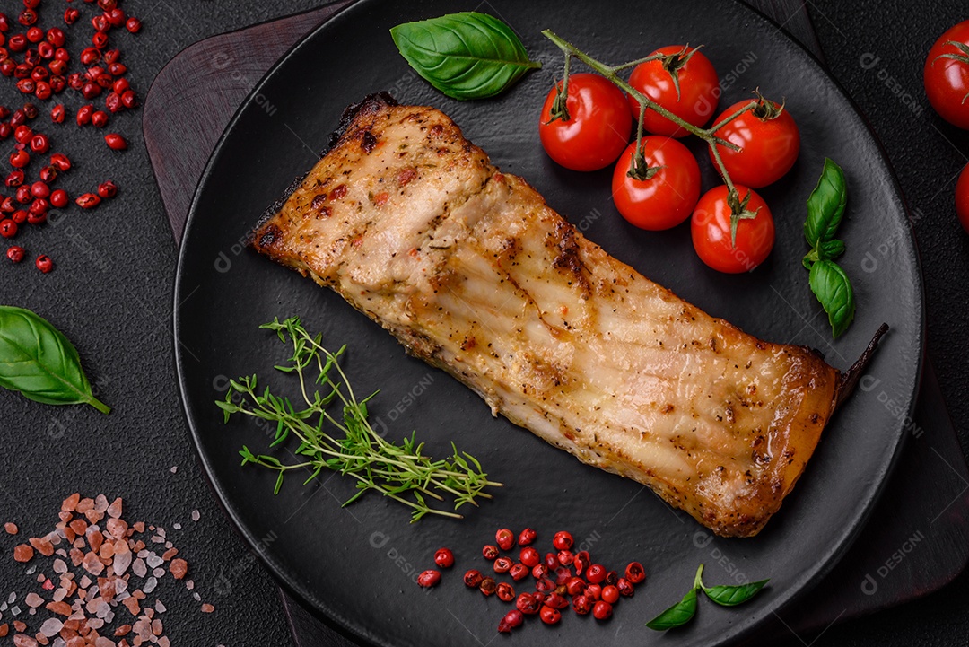 Fatia de delicioso peixe assado com sal, especiarias e ervas em uma placa cerâmica sobre um fundo escuro de concreto