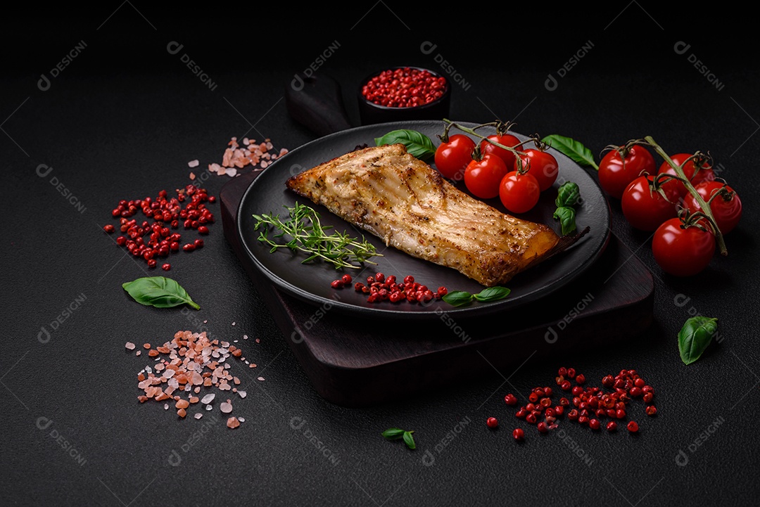 Fatia de delicioso peixe assado com sal, especiarias e ervas em uma placa cerâmica sobre um fundo escuro de concreto