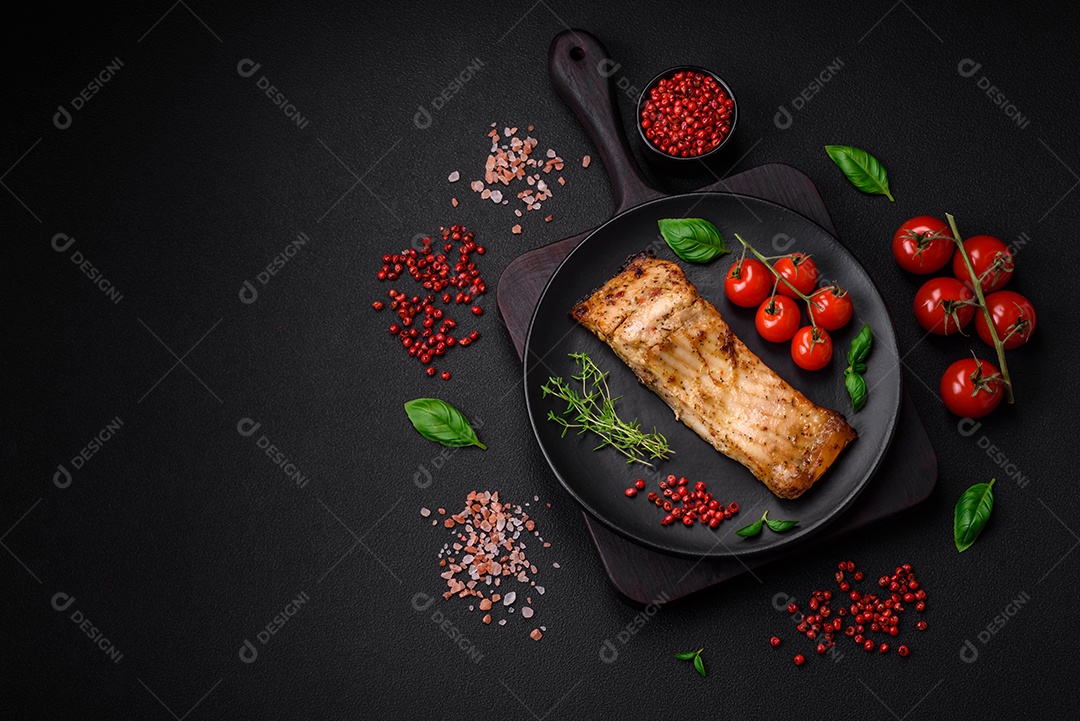 Fatia de delicioso peixe assado com sal, especiarias e ervas em uma placa cerâmica sobre um fundo escuro de concreto