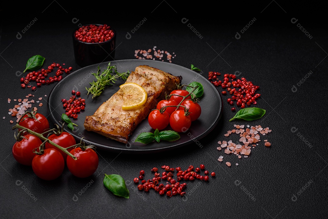 Fatia de delicioso peixe assado com sal, especiarias e ervas em uma placa cerâmica sobre um fundo escuro de concreto