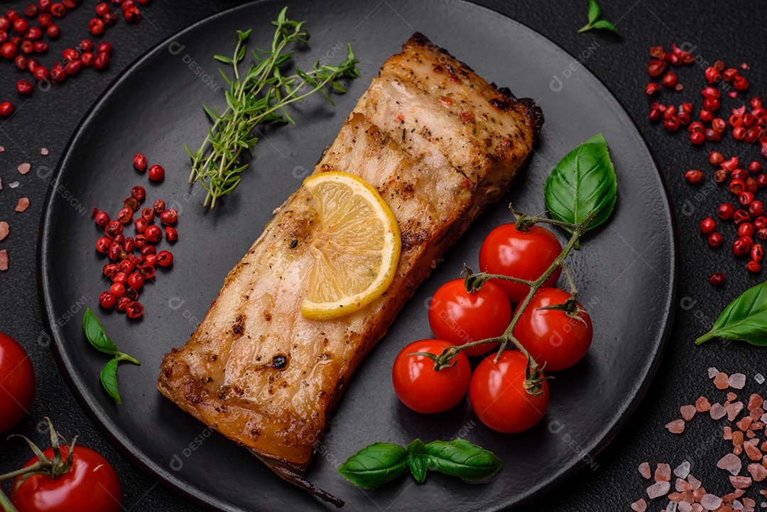 Fatia de delicioso peixe assado com sal, especiarias e ervas em uma placa cerâmica sobre um fundo escuro de concreto