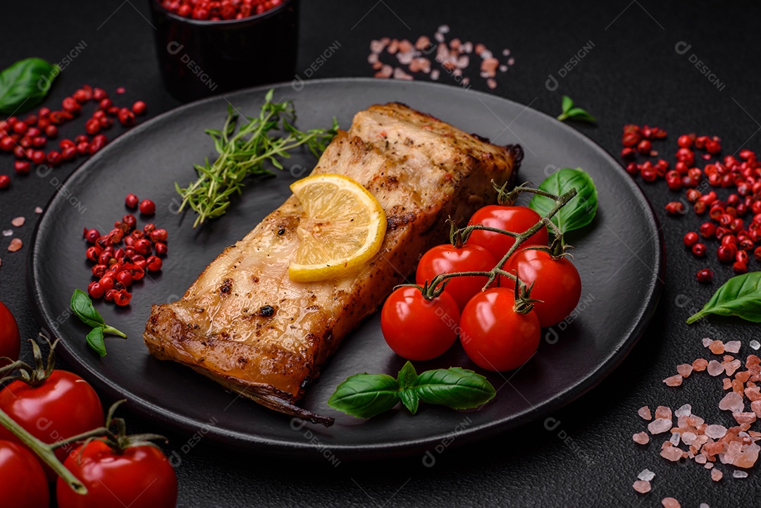 Fatia de delicioso peixe assado com sal, especiarias e ervas em uma placa cerâmica sobre um fundo escuro de concreto