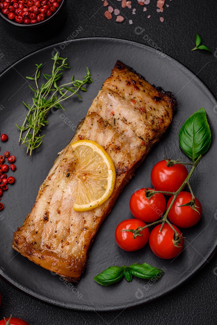 Fatia de delicioso peixe assado com sal, especiarias e ervas em uma placa cerâmica sobre um fundo escuro de concreto