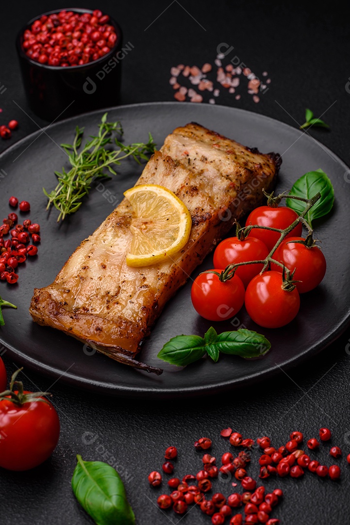 Fatia de delicioso peixe assado com sal, especiarias e ervas em uma placa cerâmica sobre um fundo escuro de concreto