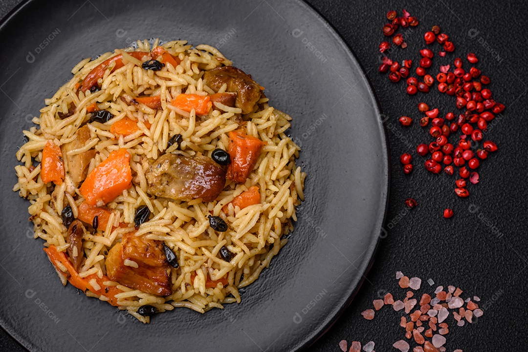 Delicioso pilaf fresco com arroz, cenoura, carne, cebola, especiarias e bagas num prato cerâmico sobre um fundo escuro de concreto