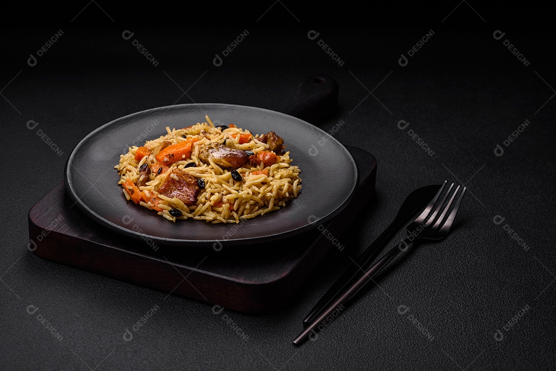 Delicioso pilaf fresco com arroz, cenoura, carne, cebola, especiarias e bagas num prato cerâmico sobre um fundo escuro de concreto