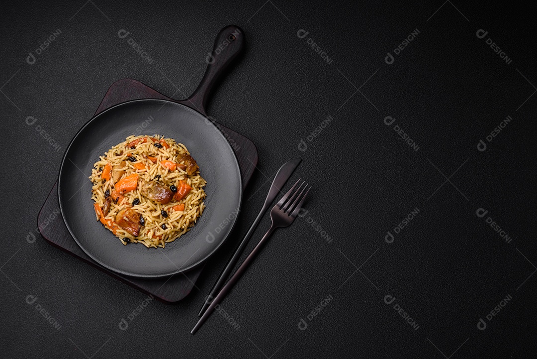 Delicioso pilaf fresco com arroz, cenoura, carne, cebola, especiarias e bagas num prato cerâmico sobre um fundo escuro de concreto