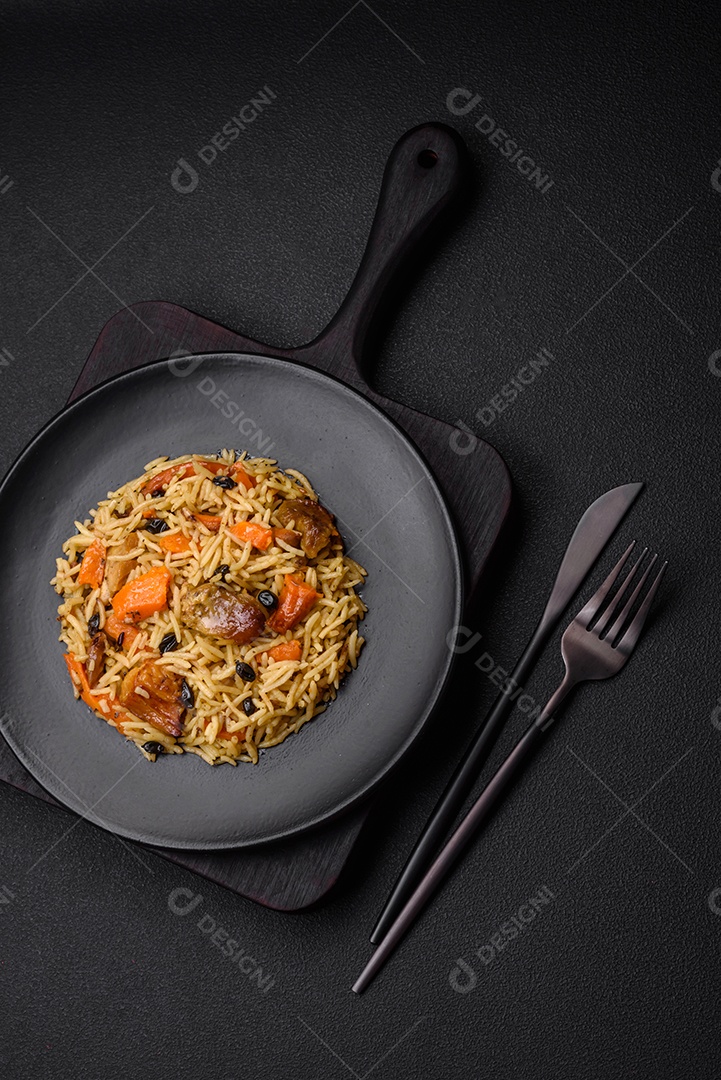 Delicioso pilaf fresco com arroz, cenoura, carne, cebola, especiarias e bagas num prato cerâmico sobre um fundo escuro de concreto