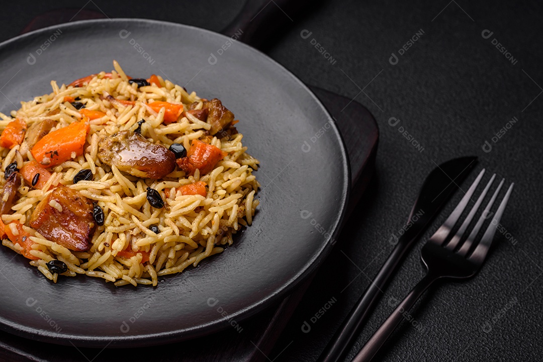 Delicioso pilaf fresco com arroz, cenoura, carne, cebola, especiarias e bagas num prato cerâmico sobre um fundo escuro de concreto