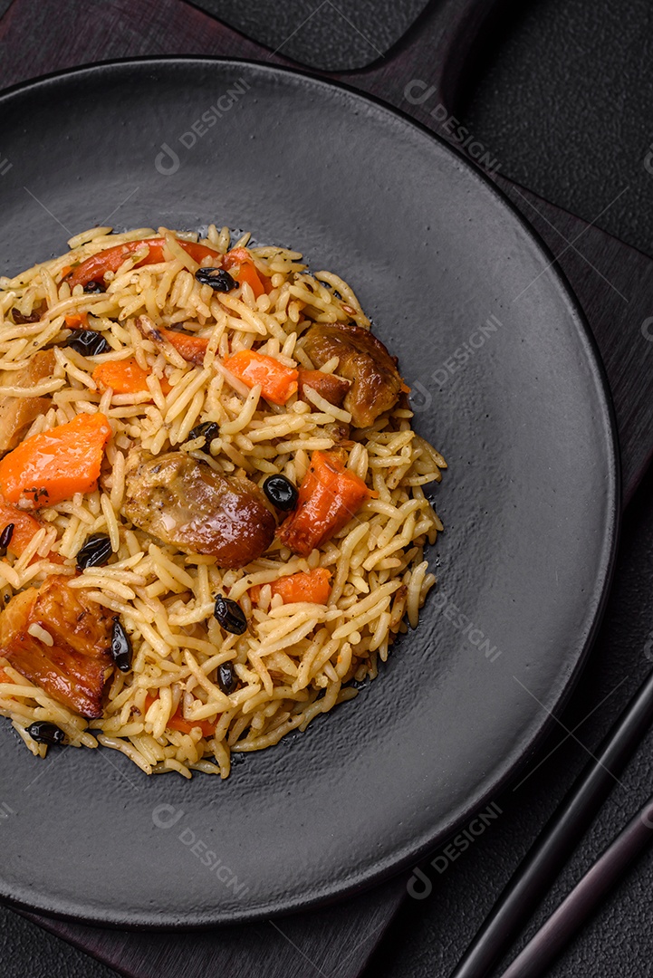 Delicioso pilaf fresco com arroz, cenoura, carne, cebola, especiarias e bagas num prato cerâmico sobre um fundo escuro de concreto