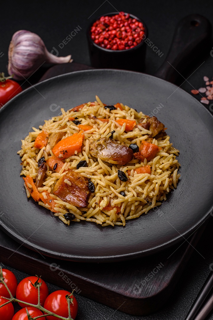Delicioso pilaf fresco com arroz, cenoura, carne, cebola, especiarias e bagas num prato cerâmico sobre um fundo escuro de concreto