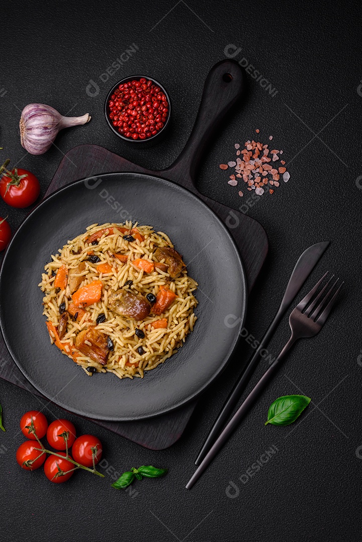 Delicioso pilaf fresco com arroz, cenoura, carne, cebola, especiarias e bagas num prato cerâmico sobre um fundo escuro de concreto