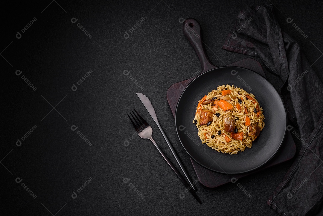 Delicioso pilaf fresco com arroz, cenoura, carne, cebola, especiarias e bagas num prato cerâmico sobre um fundo escuro de concreto