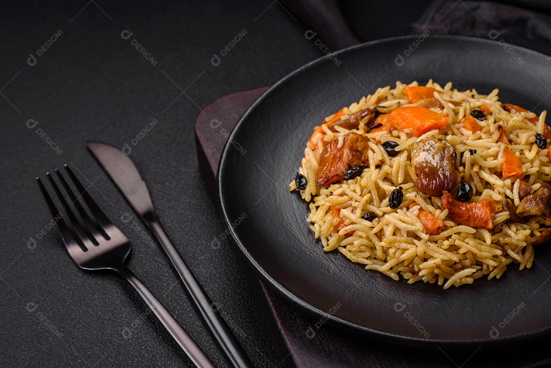 Delicioso pilaf fresco com arroz, cenoura, carne, cebola, especiarias e bagas num prato cerâmico sobre um fundo escuro de concreto