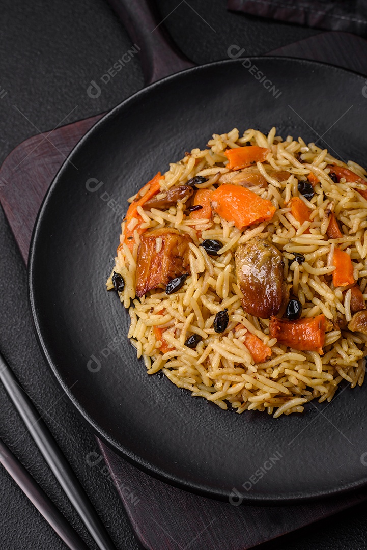 Delicioso pilaf fresco com arroz, cenoura, carne, cebola, especiarias e bagas num prato cerâmico sobre um fundo escuro de concreto