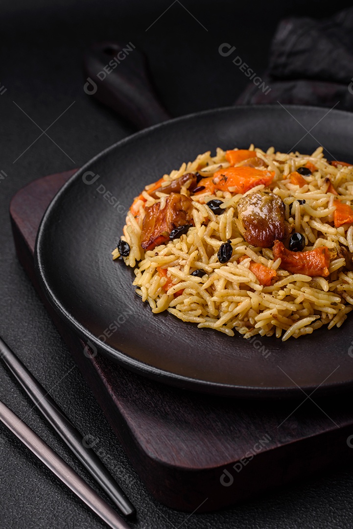 Delicioso pilaf fresco com arroz, cenoura, carne, cebola, especiarias e bagas num prato cerâmico sobre um fundo escuro de concreto