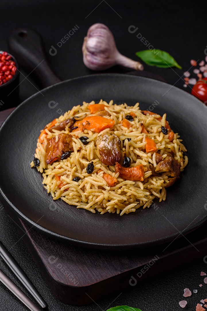 Delicioso pilaf fresco com arroz, cenoura, carne, cebola, especiarias e bagas num prato cerâmico sobre um fundo escuro de concreto