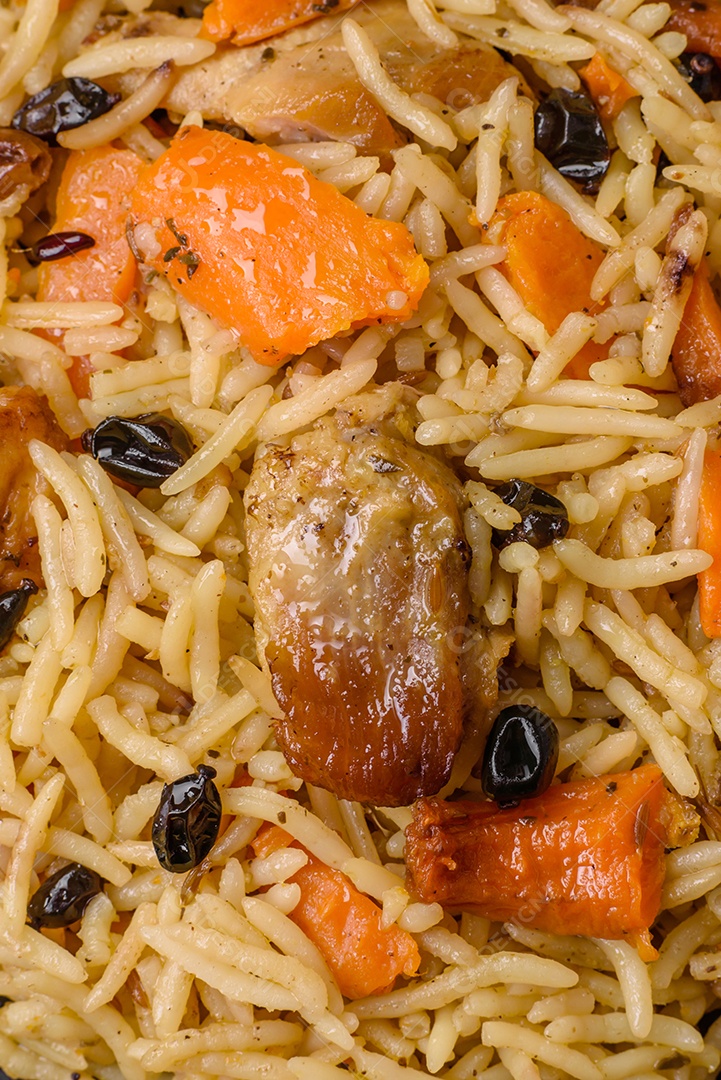 Delicioso pilaf fresco com arroz, cenoura, carne, cebola, especiarias e bagas num prato cerâmico sobre um fundo escuro de concreto