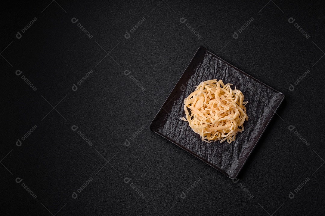 Deliciosas lulas secas em forma de lascas com sal e especiarias numa placa cerâmica sobre um fundo escuro de concreto