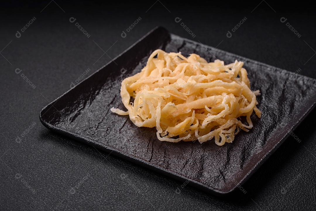 Deliciosas lulas secas em forma de lascas com sal e especiarias numa placa cerâmica sobre um fundo escuro de concreto