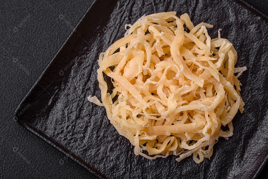 Deliciosas lulas secas em forma de lascas com sal e especiarias numa placa cerâmica sobre um fundo escuro de concreto