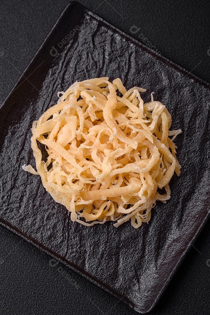 Deliciosas lulas secas em forma de lascas com sal e especiarias numa placa cerâmica sobre um fundo escuro de concreto