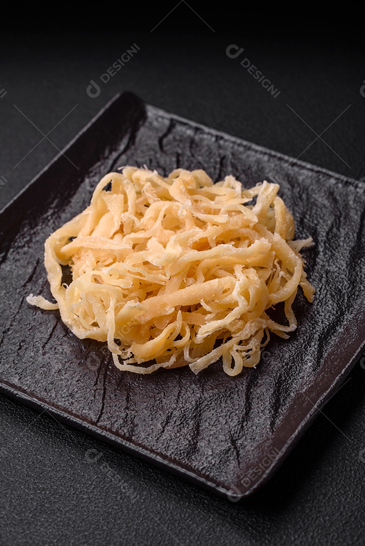 Deliciosas lulas secas em forma de lascas com sal e especiarias numa placa cerâmica sobre um fundo escuro de concreto