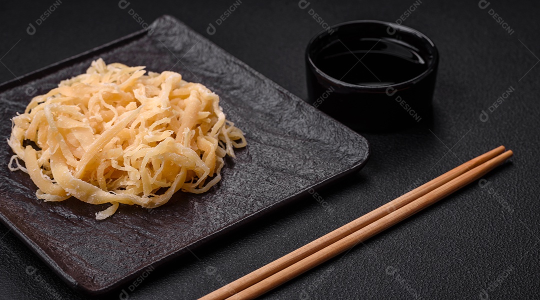 Deliciosas lulas secas em forma de lascas com sal e especiarias numa placa cerâmica sobre um fundo escuro de concreto