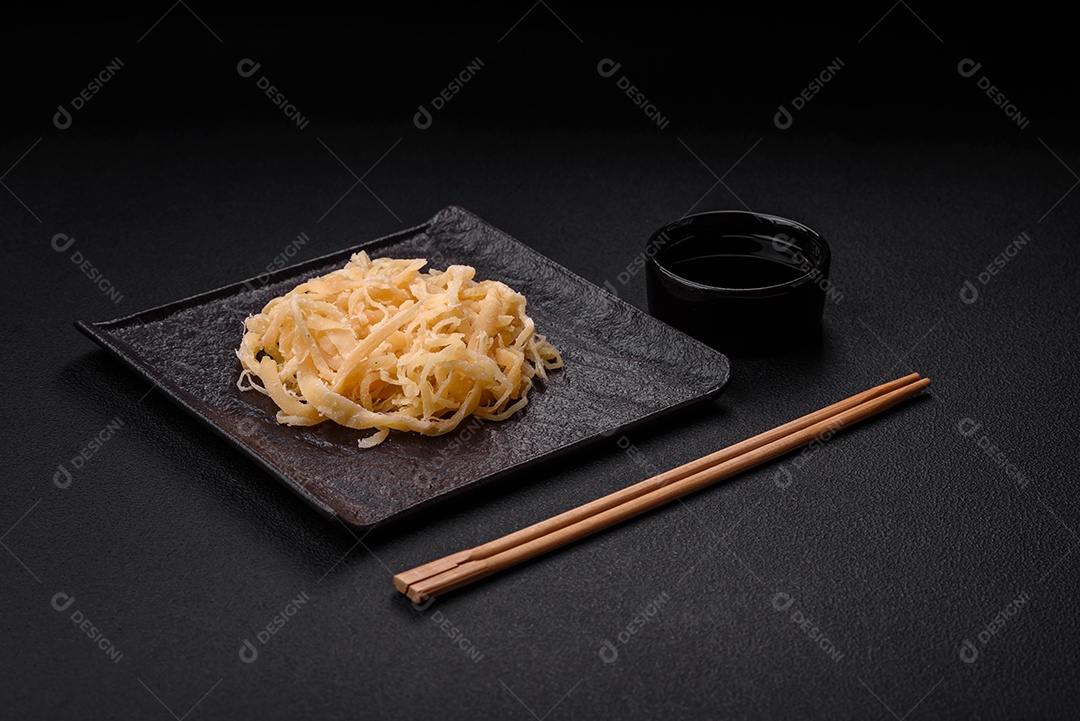 Deliciosas lulas secas em forma de lascas com sal e especiarias numa placa cerâmica sobre um fundo escuro de concreto