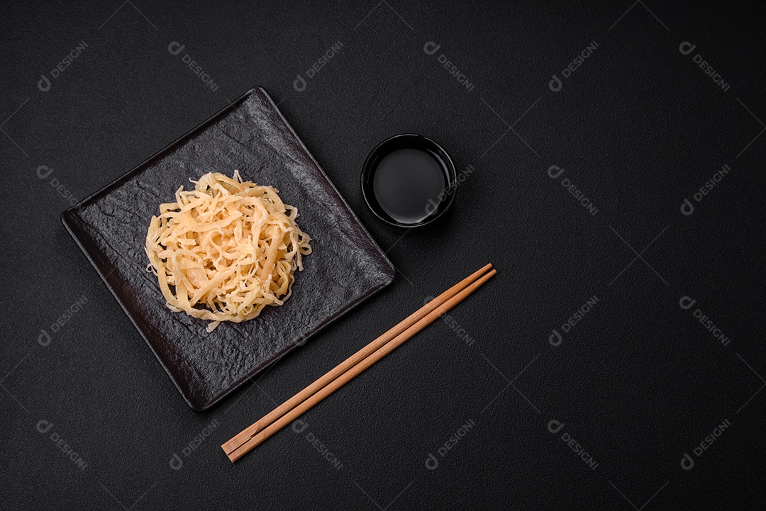 Deliciosas lulas secas em forma de lascas com sal e especiarias numa placa cerâmica sobre um fundo escuro de concreto