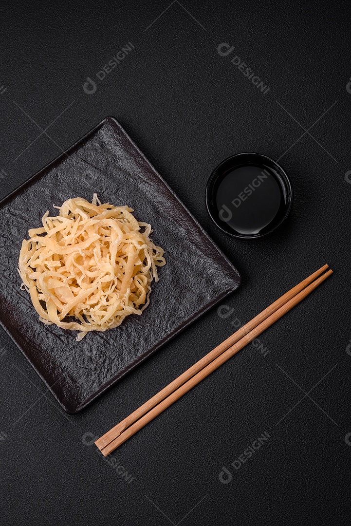 Deliciosas lulas secas em forma de lascas com sal e especiarias numa placa cerâmica sobre um fundo escuro de concreto
