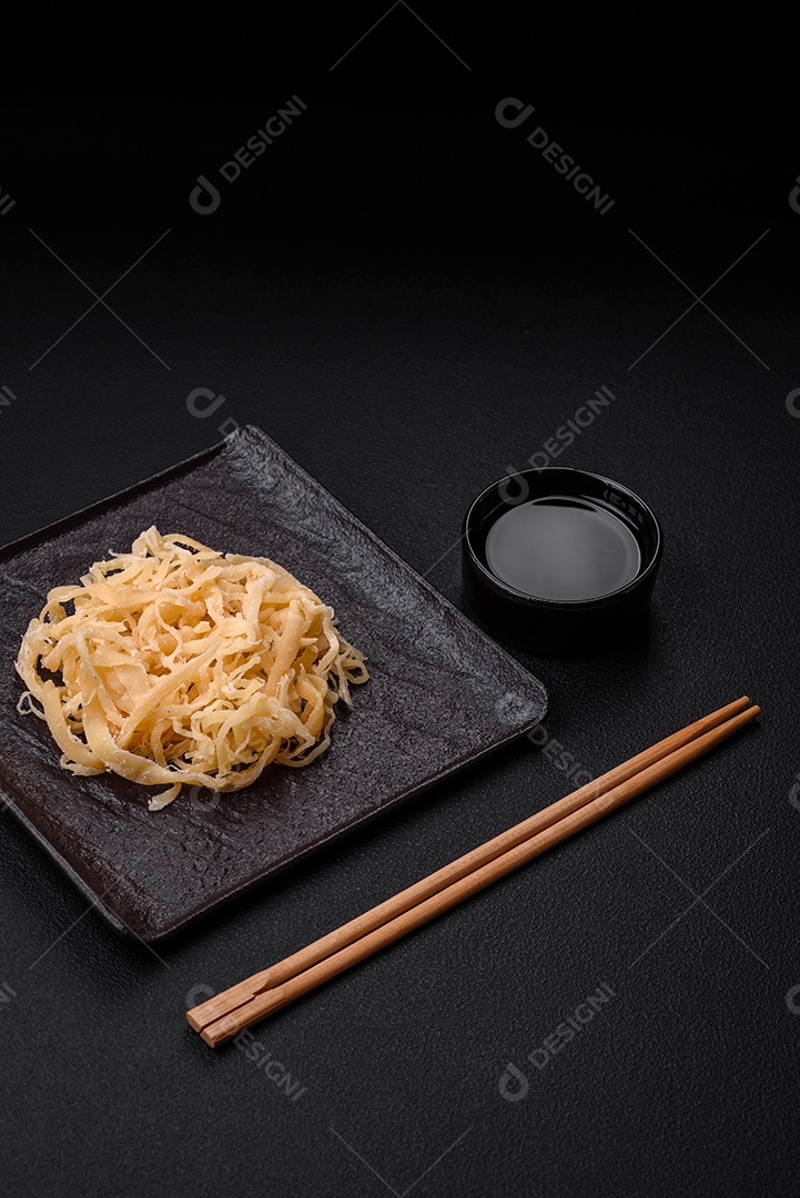 Deliciosas lulas secas em forma de lascas com sal e especiarias numa placa cerâmica sobre um fundo escuro de concreto