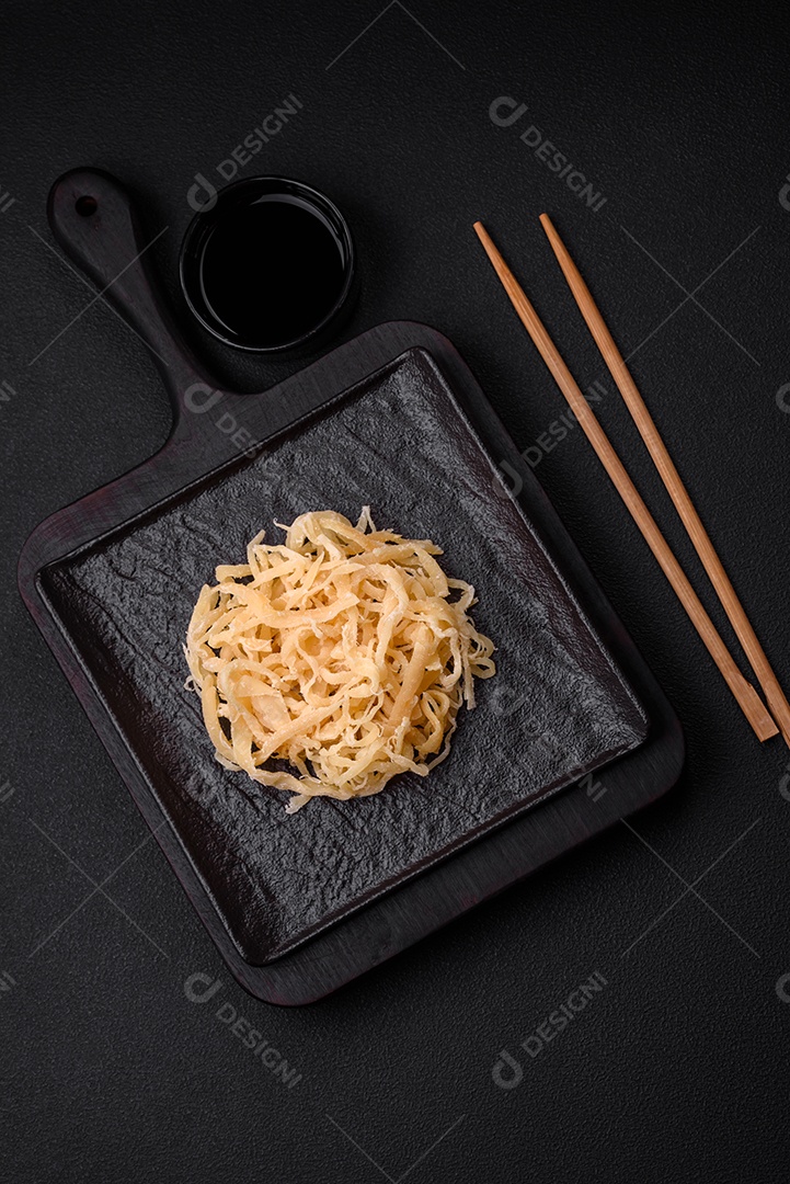 Deliciosas lulas secas em forma de lascas com sal e especiarias numa placa cerâmica sobre um fundo escuro de concreto