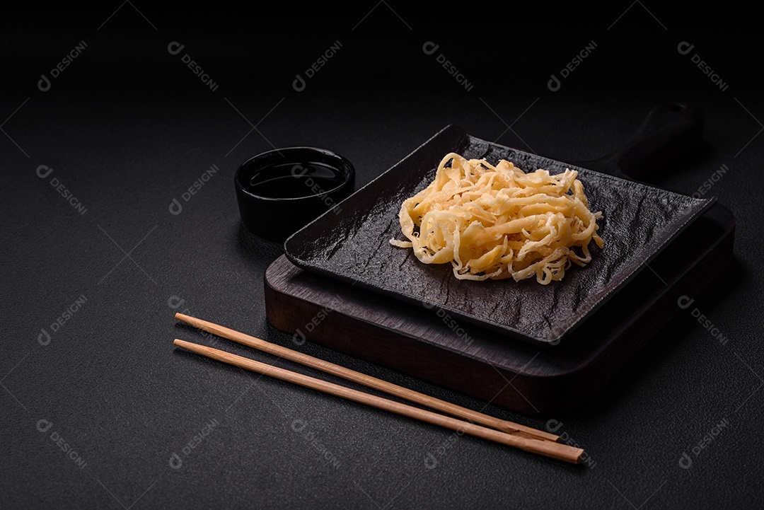 Deliciosas lulas secas em forma de lascas com sal e especiarias numa placa cerâmica sobre um fundo escuro de concreto