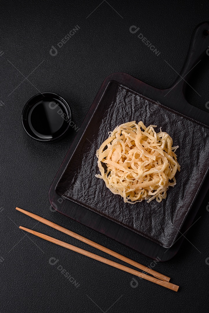 Deliciosas lulas secas em forma de lascas com sal e especiarias numa placa cerâmica sobre um fundo escuro de concreto