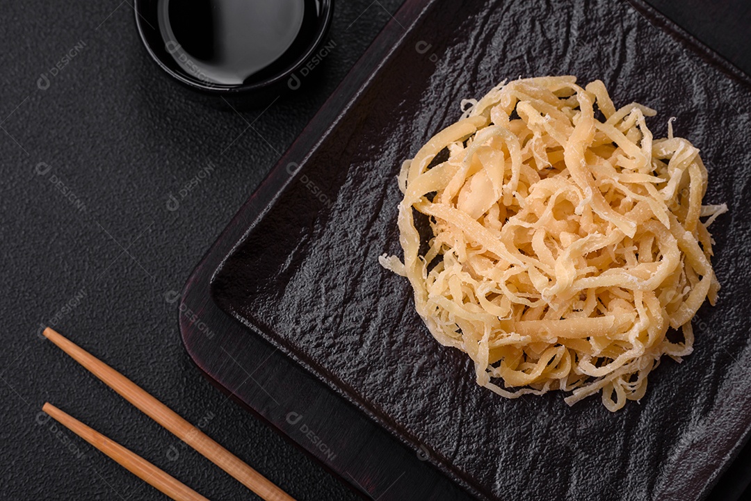 Deliciosas lulas secas em forma de lascas com sal e especiarias numa placa cerâmica sobre um fundo escuro de concreto