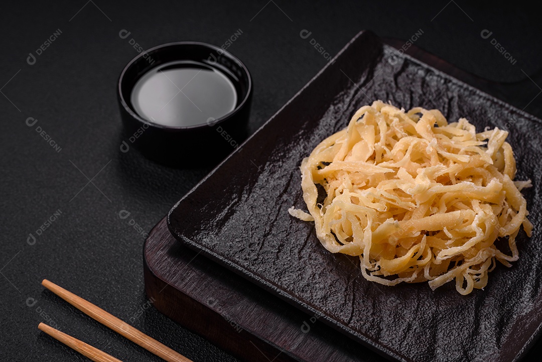 Deliciosas lulas secas em forma de lascas com sal e especiarias numa placa cerâmica sobre um fundo escuro de concreto