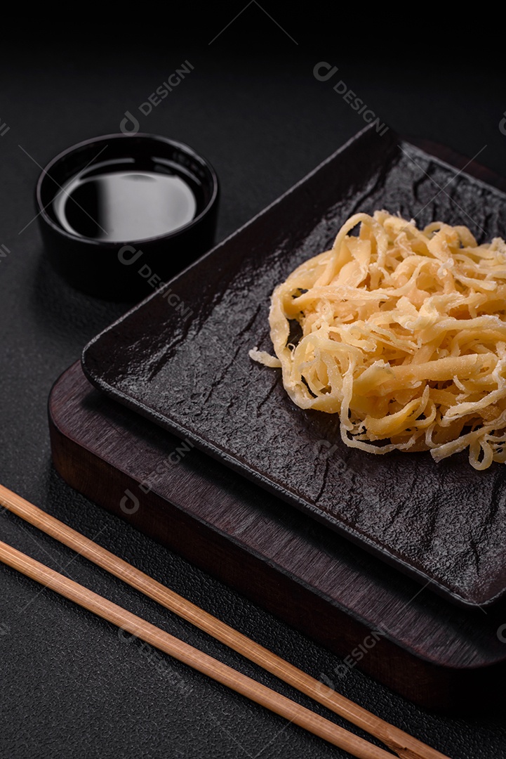 Deliciosas lulas secas em forma de lascas com sal e especiarias numa placa cerâmica sobre um fundo escuro de concreto