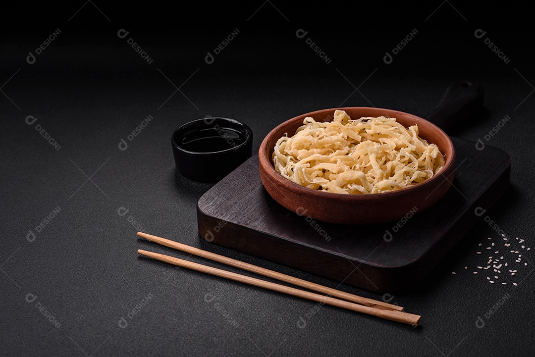 Deliciosas lulas secas em forma de lascas com sal e especiarias numa placa cerâmica sobre um fundo escuro de concreto