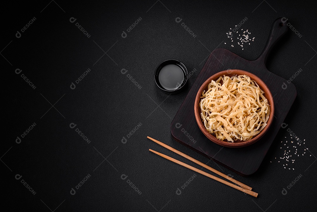 Deliciosas lulas secas em forma de lascas com sal e especiarias numa placa cerâmica sobre um fundo escuro de concreto