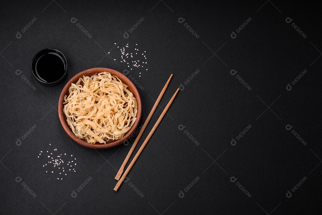 Deliciosas lulas secas em forma de lascas com sal e especiarias numa placa cerâmica sobre um fundo escuro de concreto