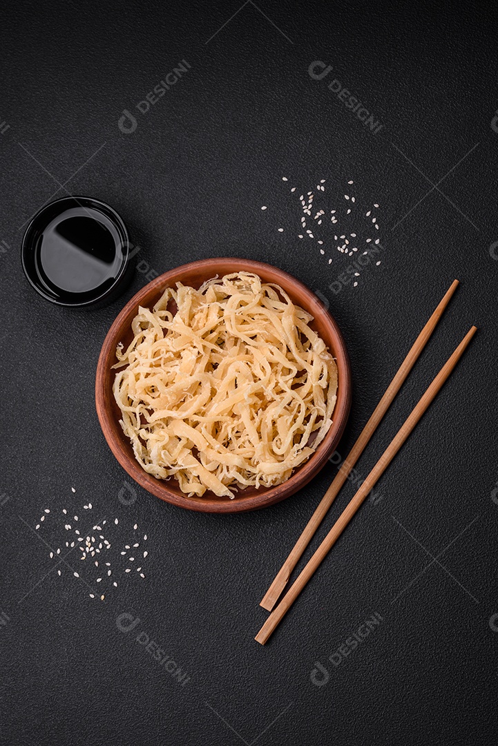 Deliciosas lulas secas em forma de lascas com sal e especiarias numa placa cerâmica sobre um fundo escuro de concreto