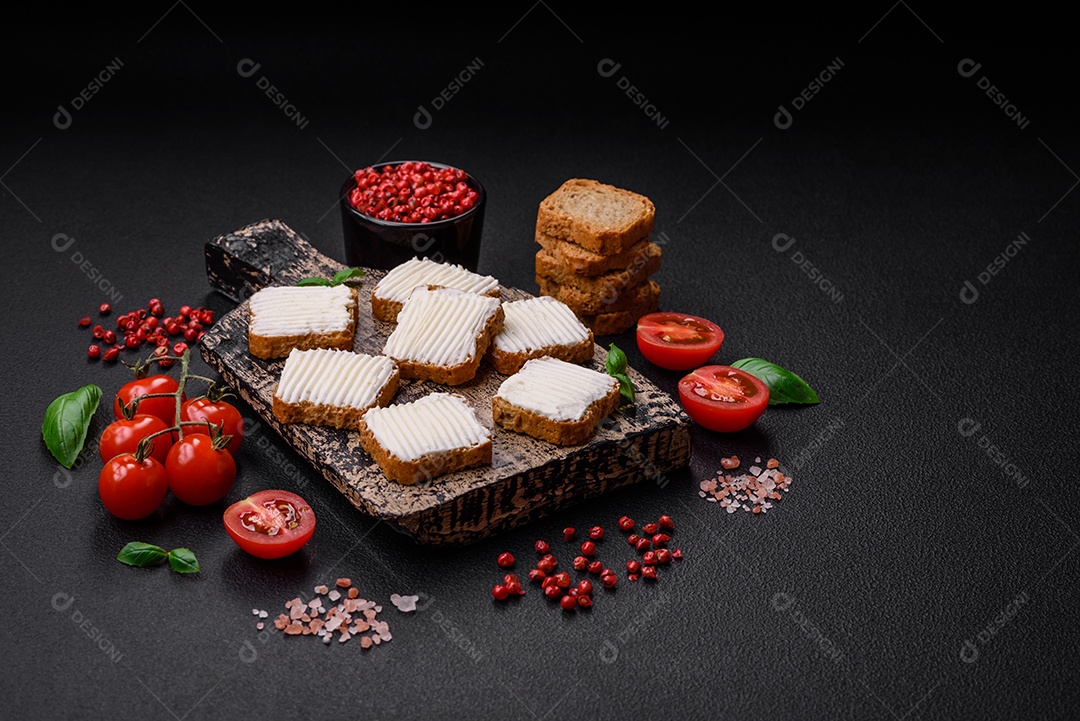 Deliciosos croutons de trigo retangulares salgados com cream cheese, tomate, sal e especiarias sobre um fundo escuro de concreto