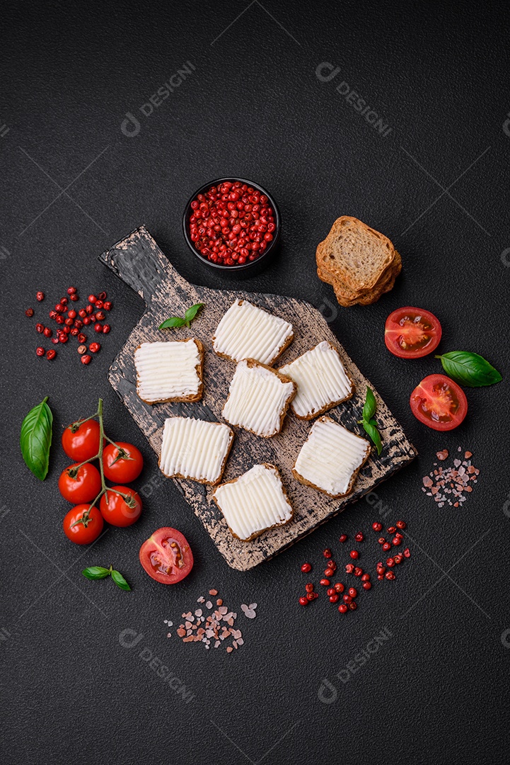 Deliciosos croutons de trigo retangulares salgados com cream cheese, tomate, sal e especiarias sobre um fundo escuro de concreto