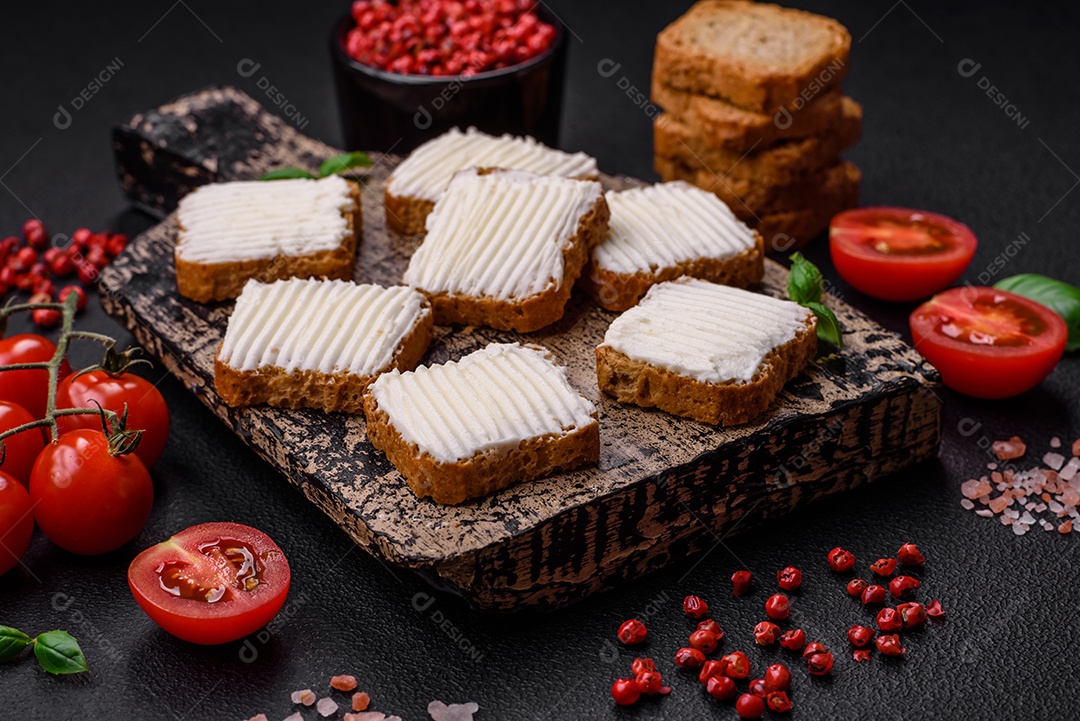Deliciosos croutons de trigo retangulares salgados com cream cheese, tomate, sal e especiarias sobre um fundo escuro de concreto