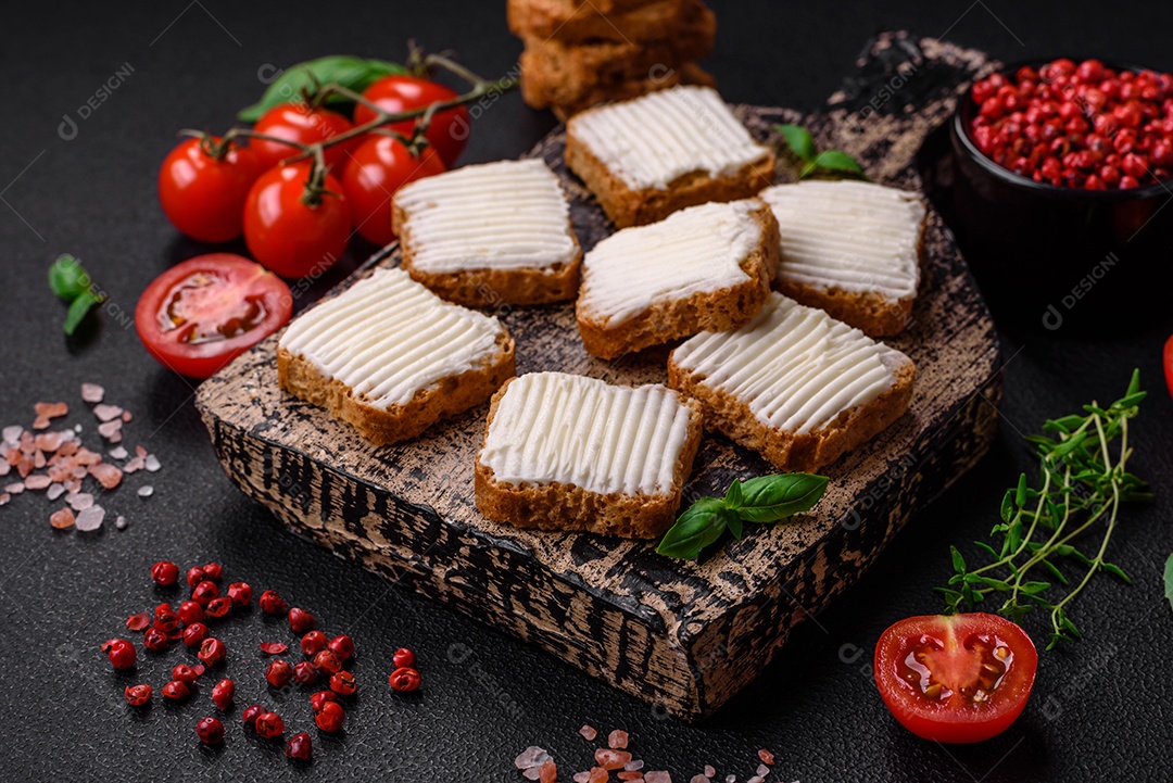 Deliciosos croutons de trigo retangulares salgados com cream cheese, tomate, sal e especiarias sobre um fundo escuro de concreto