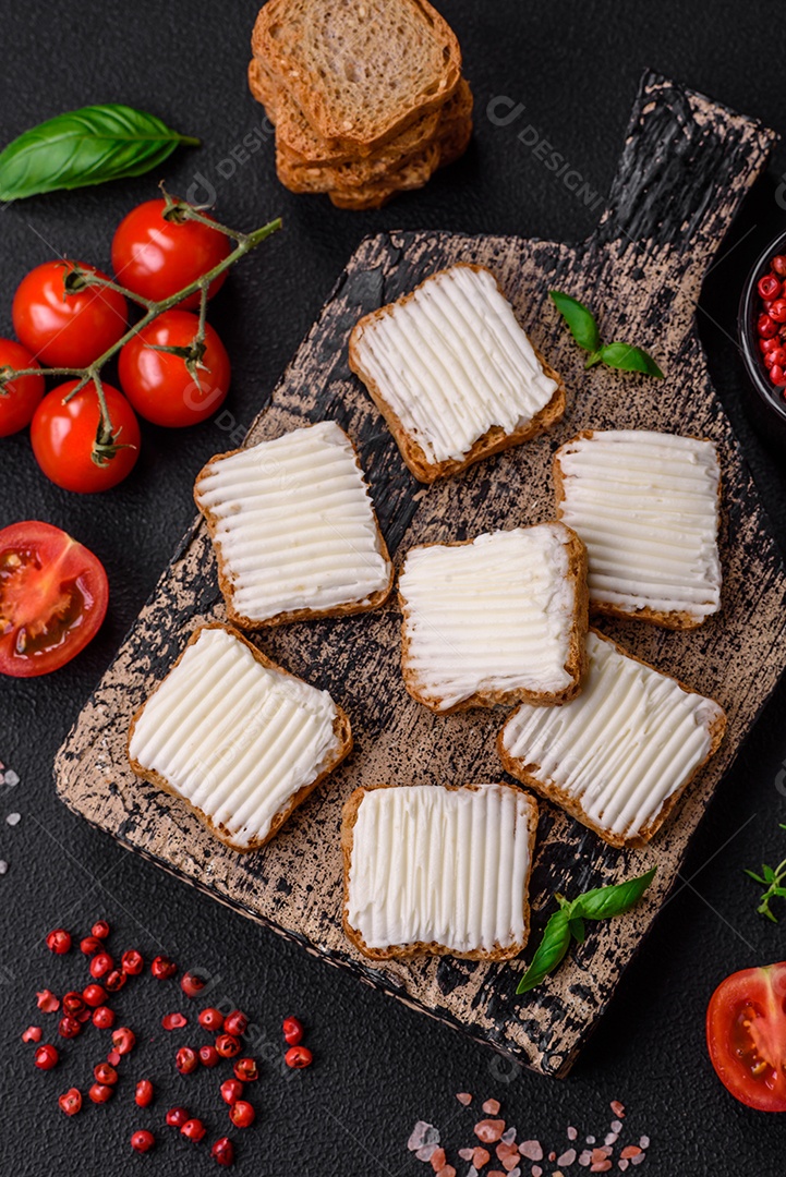 Deliciosos croutons de trigo retangulares salgados com cream cheese, tomate, sal e especiarias sobre um fundo escuro de concreto