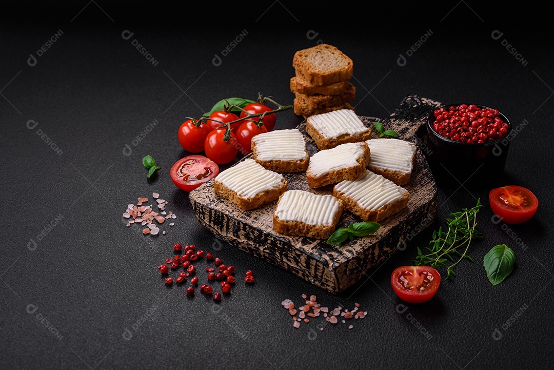 Deliciosos croutons de trigo retangulares salgados com cream cheese, tomate, sal e especiarias sobre um fundo escuro de concreto