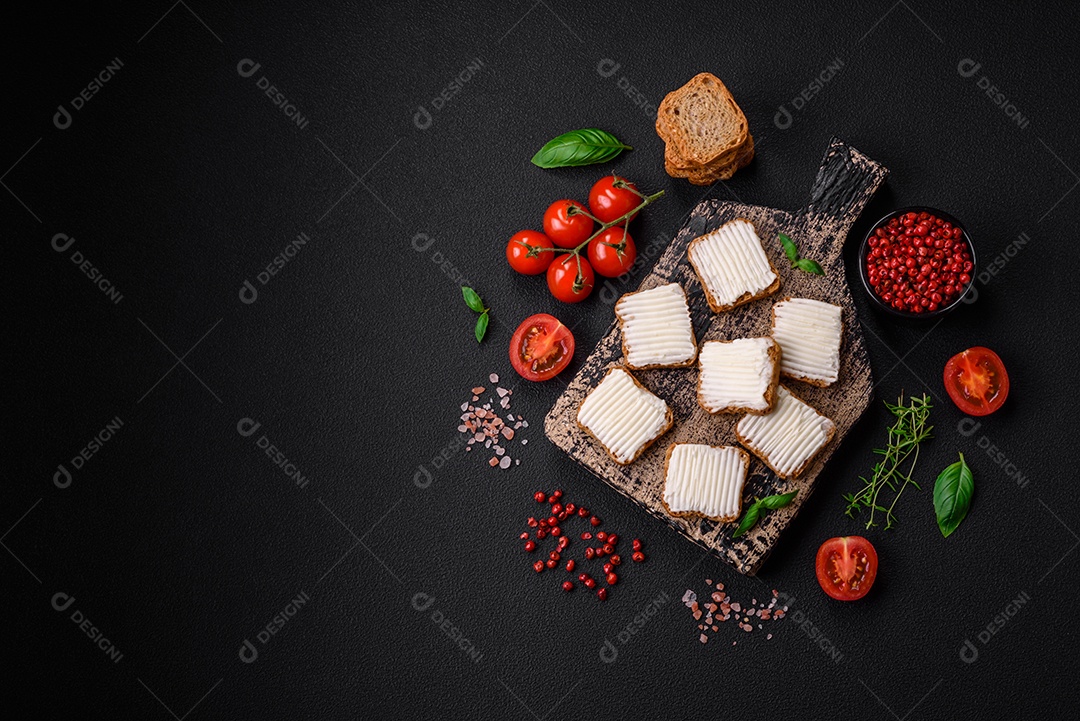 Deliciosos croutons de trigo retangulares salgados com cream cheese, tomate, sal e especiarias sobre um fundo escuro de concreto