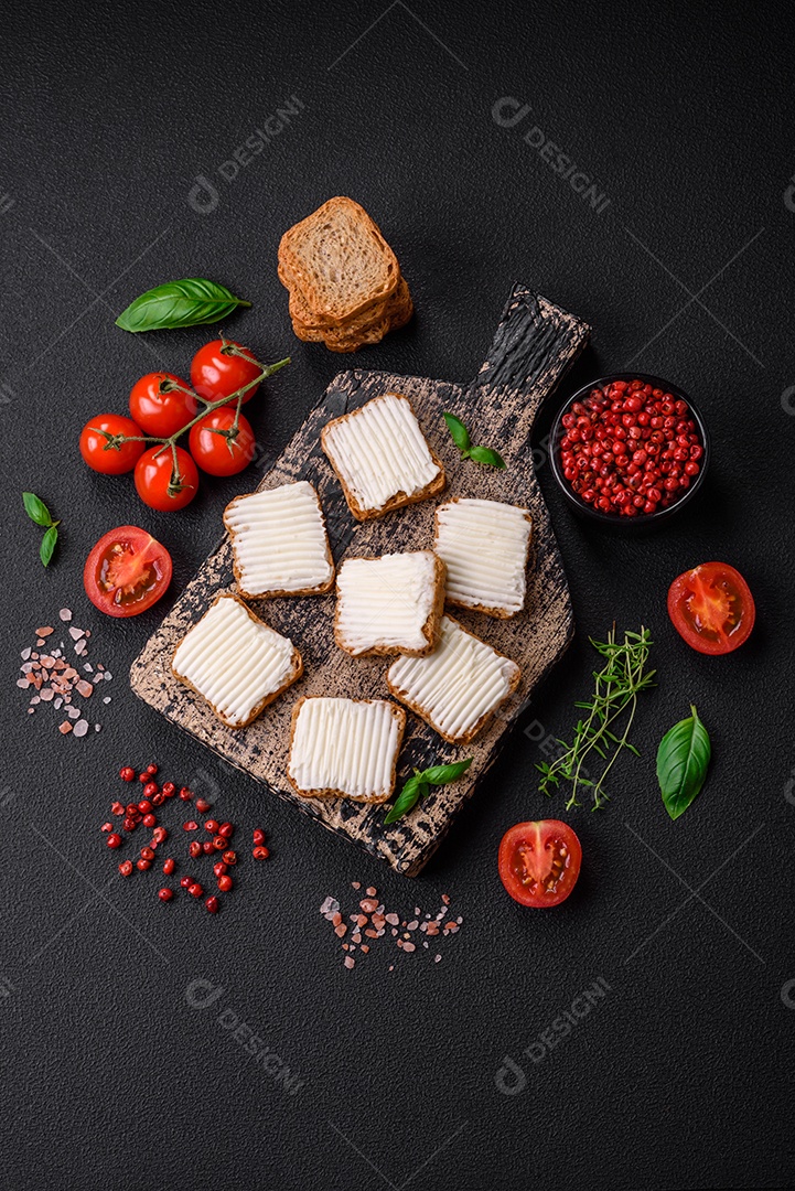 Deliciosos croutons de trigo retangulares salgados com cream cheese, tomate, sal e especiarias sobre um fundo escuro de concreto